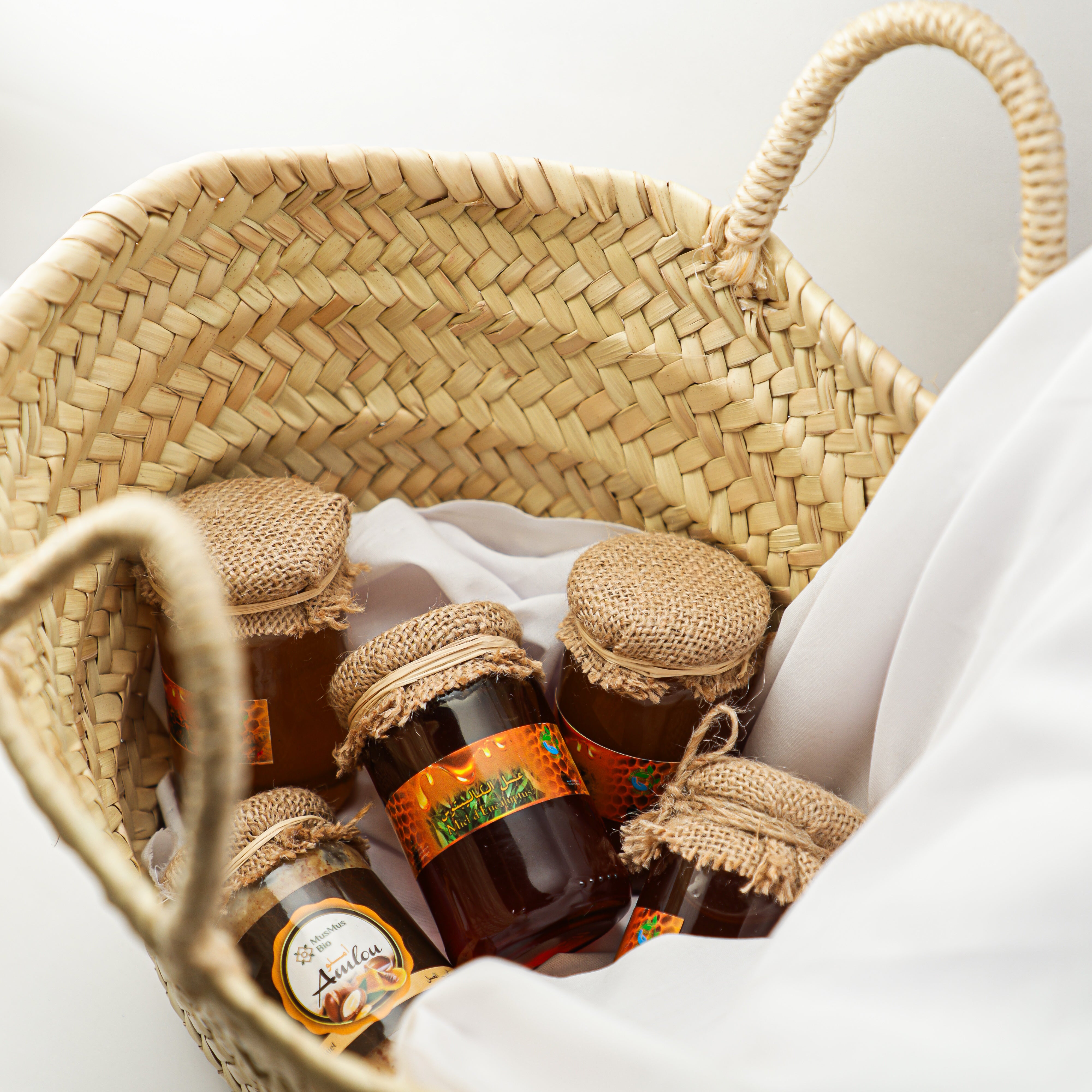 Wicker basket with jars of honey on a white background